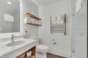 Bathroom with radiator heating unit, vanity, a tile shower, wood finished floors, and a towel warming rack