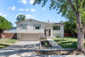 Raised ranch featuring brick siding, driveway, a garage, and a chimney