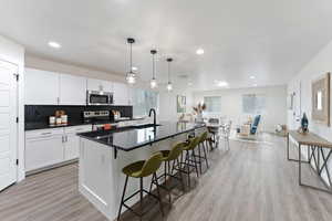 Kitchen with dark countertops, decorative backsplash, stainless steel appliances, a breakfast bar, and light wood-type flooring