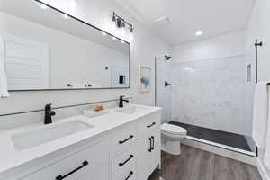 Bathroom featuring tiled shower, wood finished floors, and double vanity
