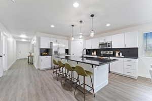 Kitchen with dark countertops, tasteful backsplash, appliances with stainless steel finishes, a breakfast bar, and light wood-style flooring