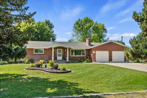 Ranch-style home featuring an attached garage, a chimney, concrete driveway, and a front lawn