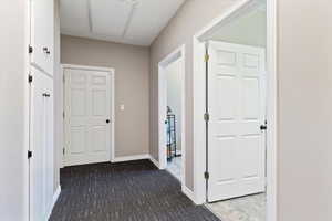 Hallway featuring dark colored carpet and baseboards