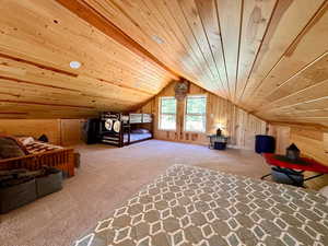 Bedroom with wood walls, vaulted ceiling, wooden ceiling, and carpet flooring