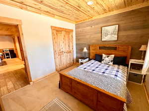 Bedroom with wood ceiling, wooden walls, carpet, and a closet