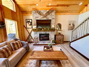 Living area featuring wooden ceiling, wood finished floors, a stone fireplace, vaulted ceiling, and stairs