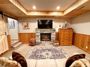 Carpeted living room with wood walls, a wainscoted wall, a barn door, a fireplace, and recessed lighting