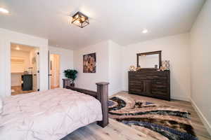 Bedroom with light wood-style floors, recessed lighting, and connected bathroom