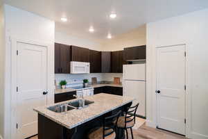 Kitchen with white appliances, light wood-style floors, dark brown cabinets, a kitchen breakfast bar, and recessed lighting