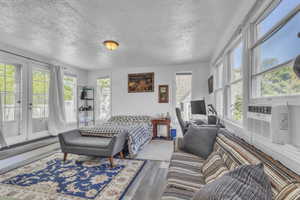 Bedroom featuring access to outside, wood finished floors, french doors, a textured ceiling, and cooling unit