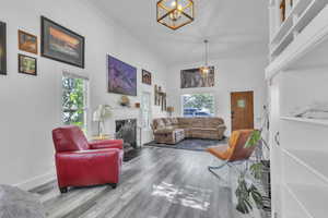 Living area featuring a chandelier, ornamental molding, wood finished floors, and a fireplace with flush hearth