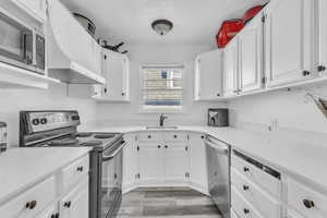 Kitchen with stainless steel appliances, extractor fan, a textured ceiling, white cabinetry, and light wood-type flooring