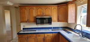 Kitchen featuring stainless steel microwave, brown cabinets, light tile patterned floors, and tile counters
