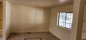 Tiled empty room featuring a textured ceiling and baseboards