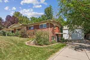 View of front facade featuring brick siding, concrete driveway, an outbuilding, and a front yard