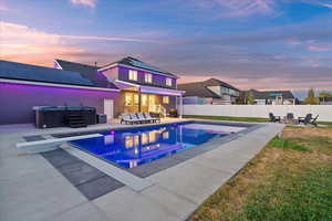 Pool at dusk featuring a hot tub, an outdoor fire pit, a patio, a diving board, and a fenced backyard