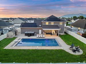 Back of house at dusk featuring a fenced backyard, an outdoor living space with a fire pit, a patio area, and roof mounted solar panels