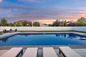 Pool at dusk with an outdoor fire pit, a fenced backyard, and a patio
