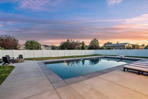 Pool at dusk with a patio area, a fire pit, a fenced backyard, and a diving board