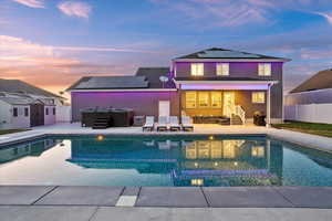Back of house at dusk with a hot tub, roof mounted solar panels, a patio area, a storage shed, and a fenced backyard