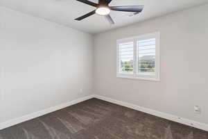 Empty room featuring dark colored carpet and ceiling fan