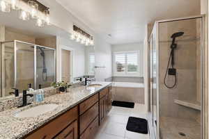 Full bathroom featuring a stall shower, a bath, double vanity, a textured ceiling, and tile patterned floors