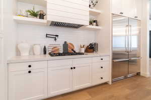 Kitchen with open shelves, tasteful backsplash, stainless steel built in fridge, light wood-type flooring, and light countertops
