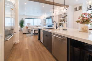 Kitchen with stainless steel dishwasher, built in fridge, light wood-type flooring, light stone counters, and hanging light fixtures