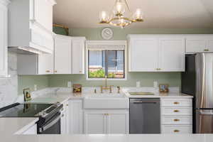 Kitchen with appliances with stainless steel finishes, white cabinets, custom exhaust hood, a chandelier, and light countertops