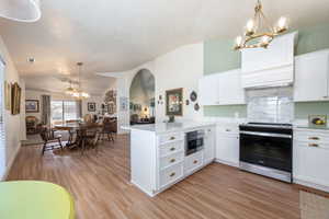 Kitchen featuring a chandelier, a peninsula, stainless steel range with electric cooktop, lofted ceiling, and backsplash