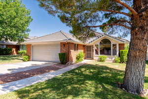 Ranch-style house featuring brick siding, a garage, a tiled roof, a front yard, and concrete driveway