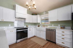 Kitchen with lofted ceiling, appliances with stainless steel finishes, a chandelier, white cabinets, and wood finished floors