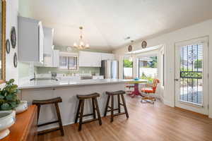 Kitchen featuring lofted ceiling, a peninsula, a chandelier, plenty of natural light, and light wood-style flooring