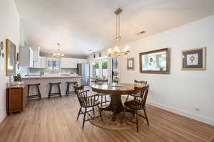 Dining room with a chandelier, vaulted ceiling, and light wood-style floors
