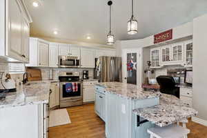 Kitchen featuring appliances with stainless steel finishes, a center island, decorative backsplash, light wood-type flooring, and white cabinets