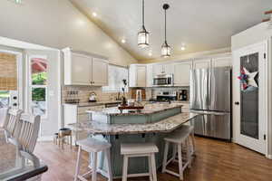 Kitchen featuring stainless steel appliances, decorative backsplash, a kitchen bar, a kitchen island, and high vaulted ceiling