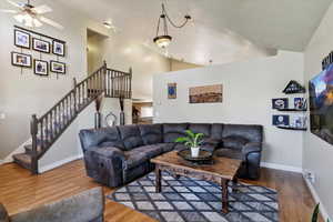 Living area with ceiling fan, stairs, wood finished floors, and high vaulted ceiling