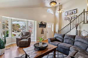Living area featuring light wood-style floors, ceiling fan, stairway, and high vaulted ceiling