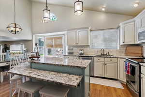 Kitchen featuring lofted ceiling, stainless steel appliances, backsplash, a kitchen island, and light wood-style flooring