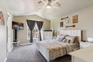 Bedroom featuring carpet flooring, lofted ceiling, ceiling fan, a textured ceiling, and a wood stove