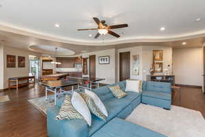 Living room featuring dark wood finished floors, a raised ceiling, recessed lighting, and a ceiling fan