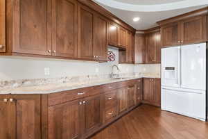 Kitchen featuring white refrigerator with ice dispenser, dark wood finished floors, light stone counters, and recessed lighting