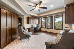 Home office with built in study area, light wood-style floors, ceiling fan, and a raised ceiling