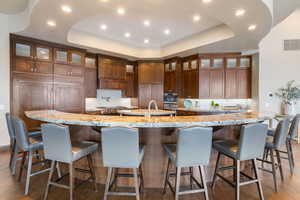 Kitchen featuring dark wood-style floors, a tray ceiling, recessed lighting, backsplash, and a large island with sink