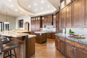 Kitchen featuring a large island with sink, hardwood / wood-style floors, recessed lighting, a breakfast bar, and a tray ceiling
