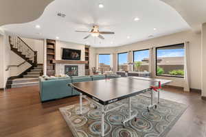 Rec room featuring a ceiling fan, a glass covered fireplace, hardwood / wood-style flooring, recessed lighting, and built in shelves
