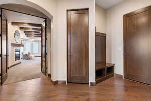 Mudroom with beamed ceiling, dark wood-style floors, arched walkways, a glass covered fireplace, and dark carpet