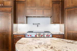 Kitchen with tasteful backsplash, luxury stove, brown cabinetry, and light stone counters