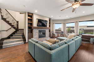 Living room with a glass covered fireplace, stairs, hardwood / wood-style flooring, a ceiling fan, and recessed lighting
