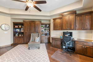 Office area with built in study area, dark wood finished floors, and ceiling fan